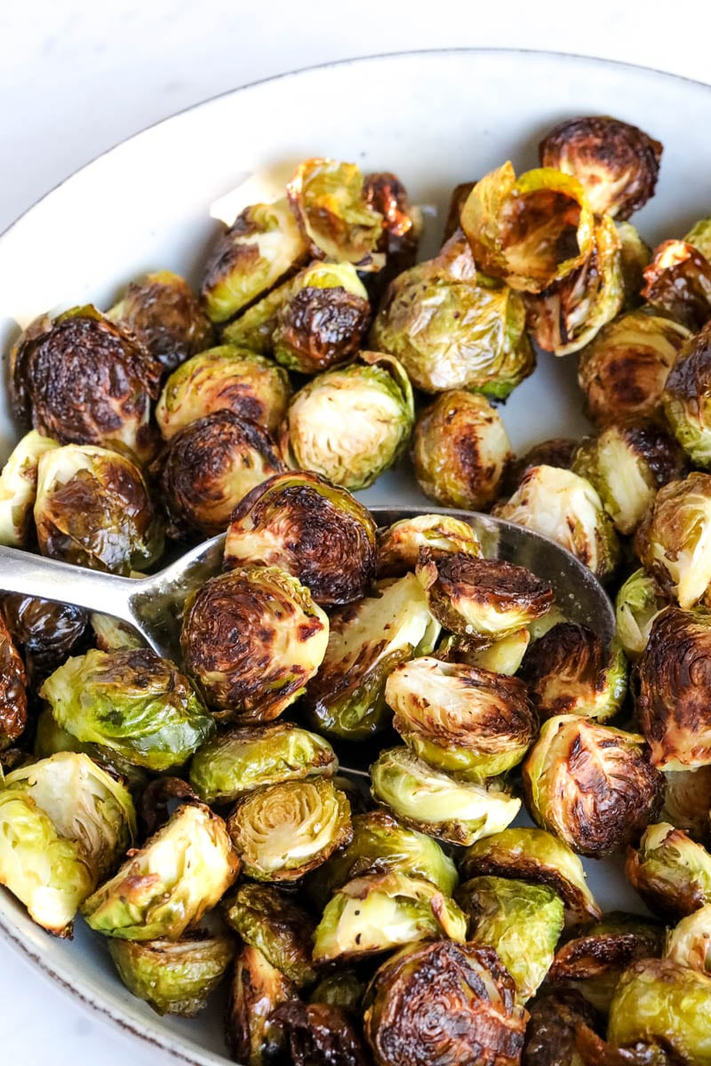 Spoon scooping oven roasted brussels sprouts from bowl.