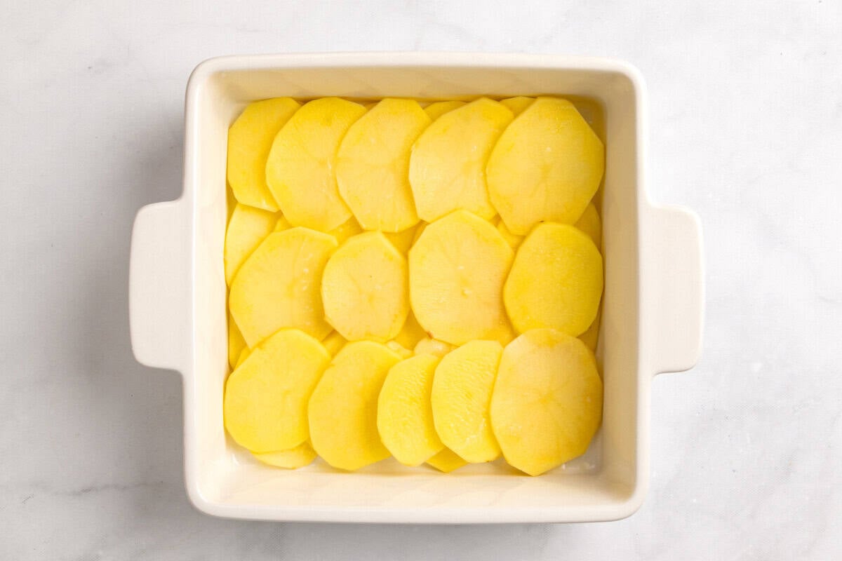 Sliced potatoes arranged in baking dish.