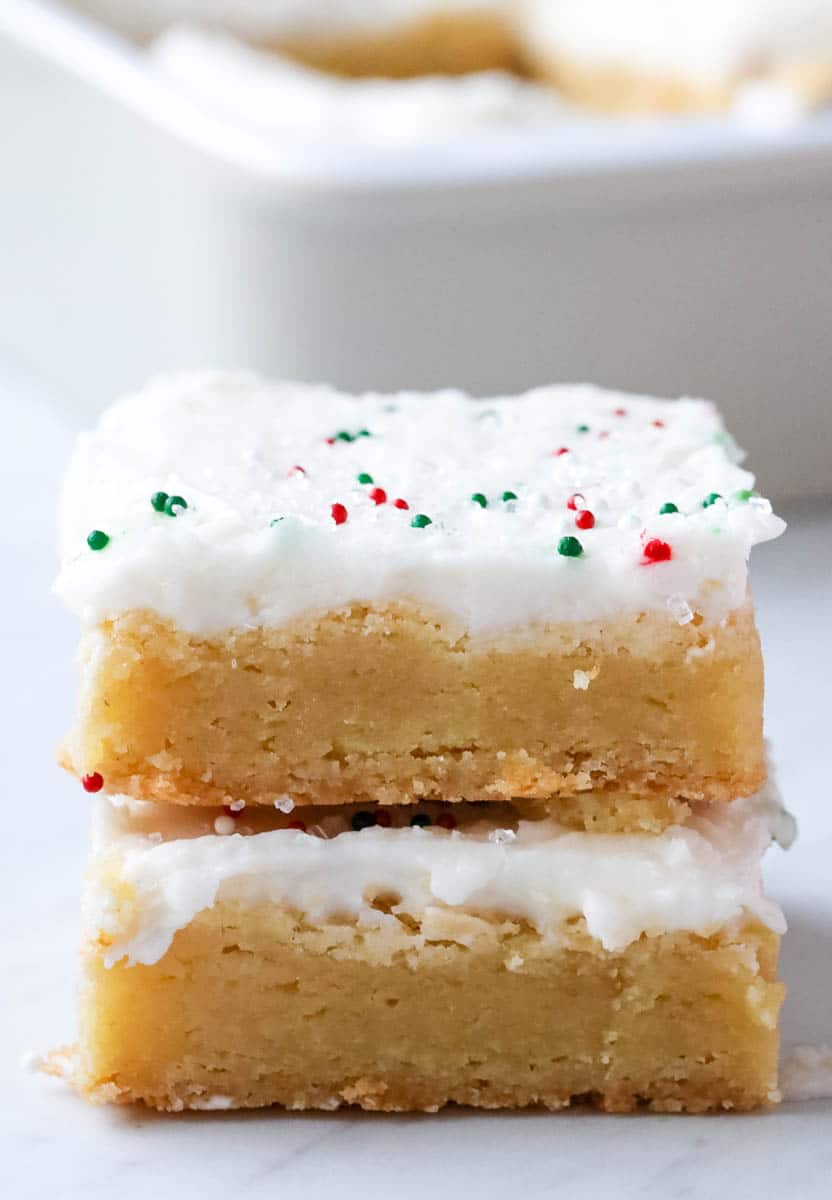 sugar cookie bars stacked on top of each other with frosting and sprinkles on top 