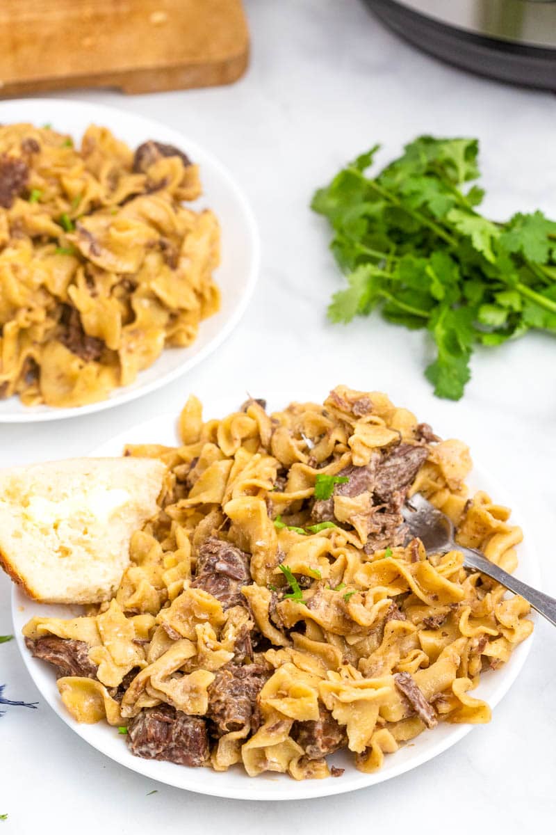 top shot of pasta and meat on white plate with buttered bread