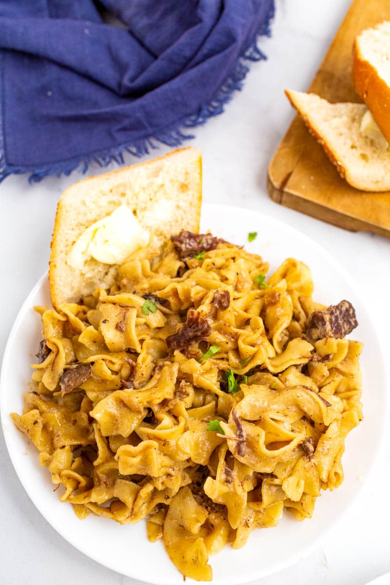 top shot of beef stroganoff on white plate with buttered bread