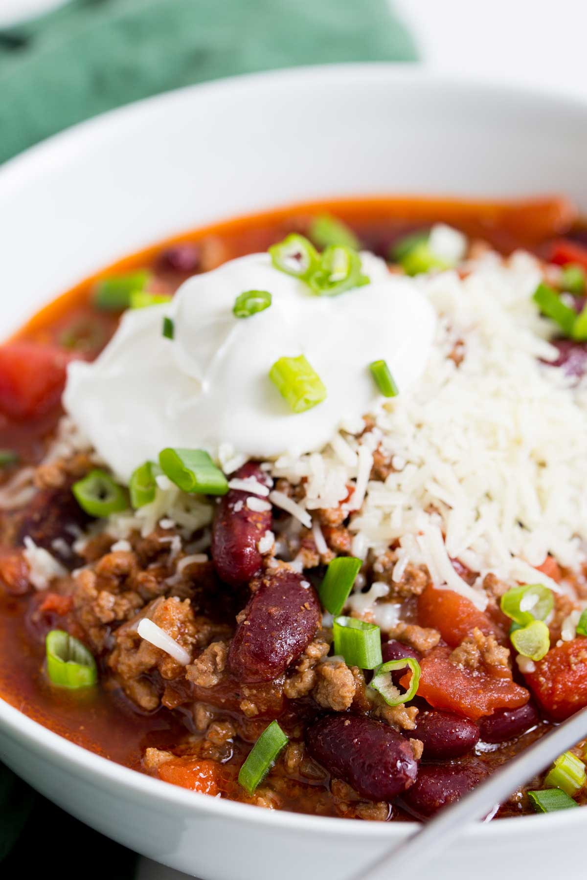crockpot chili served in a white round bowl topped with cheese, sour cream and slived green onions