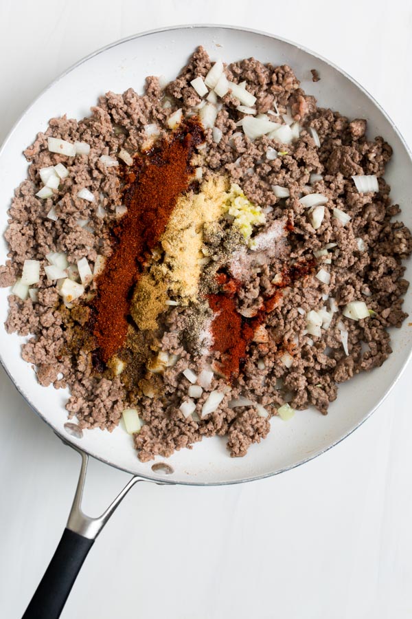 adding the spices to the skillet of ground beef 