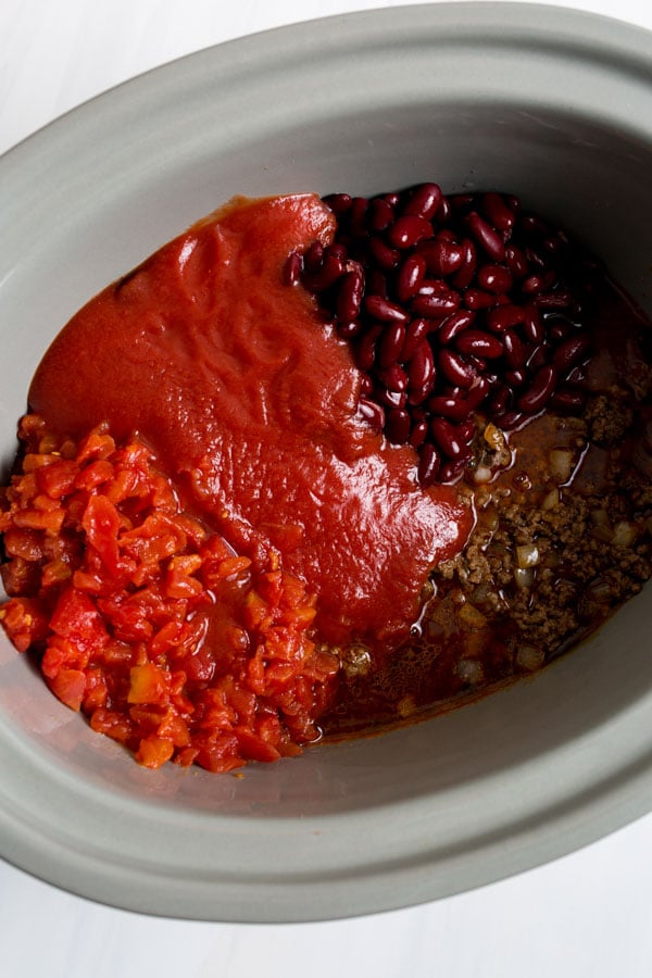 adding all the ingredients to make chili into the crock pot 