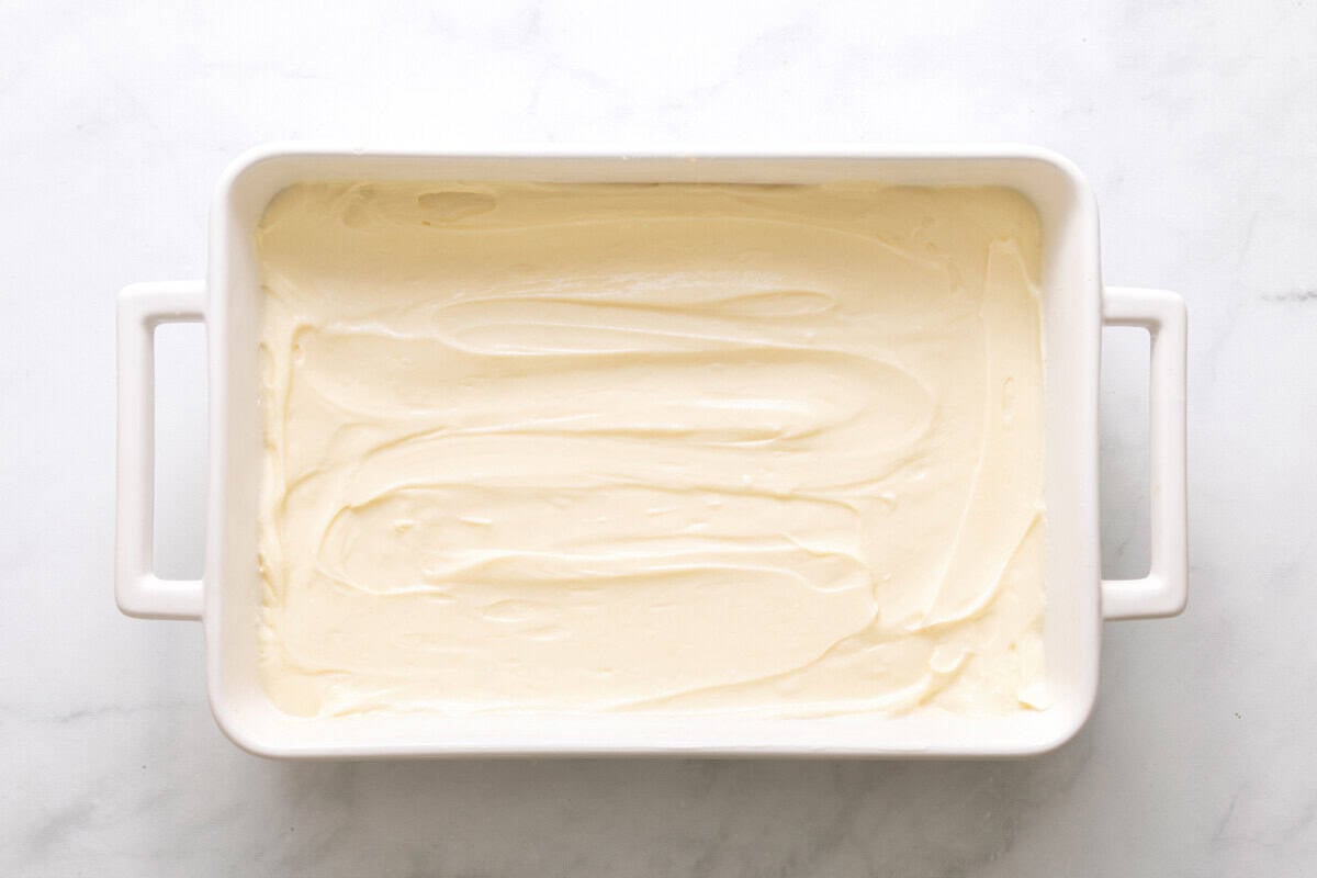 Cheesecake filling spread over crust in baking dish.