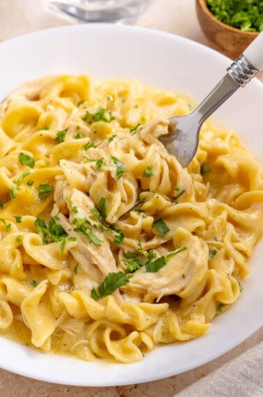 A fork digs into a bowl of crockpot chicken and noodles.