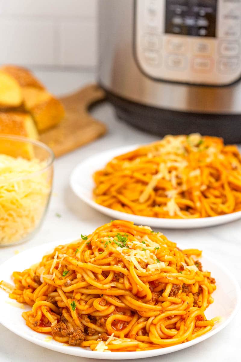 Spaghetti with red sauce and ground beef on a white plate next to Instant Pot.