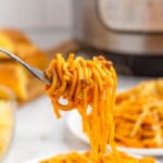 fork with noodles wrapped around it above white plate of instant pot spaghetti