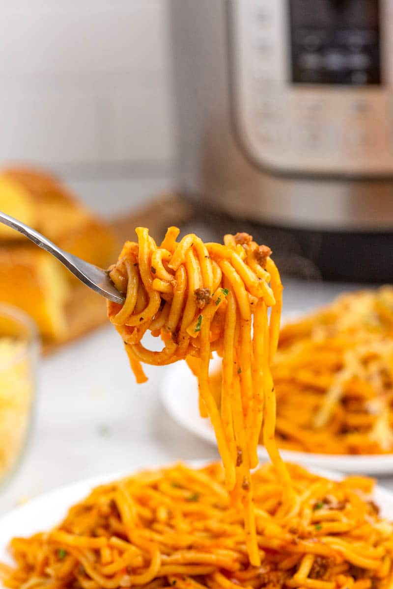 Fork with noodles wrapped around it above white plate of instant pot spaghetti.