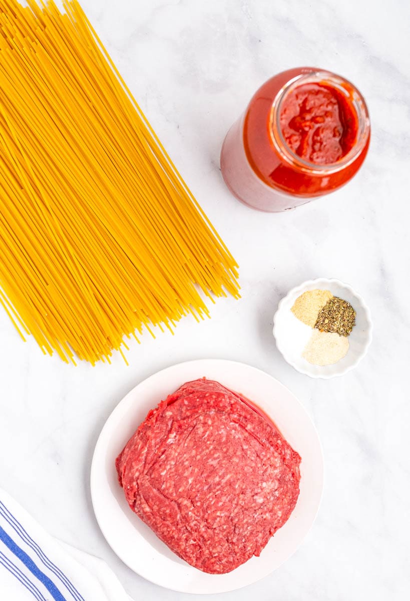 Top shot of ingredients for spaghetti laid out on a white countertop.