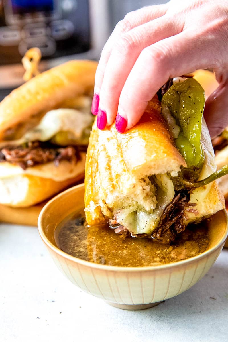 hand holding a mississippi sandwich and dipping it into au jus