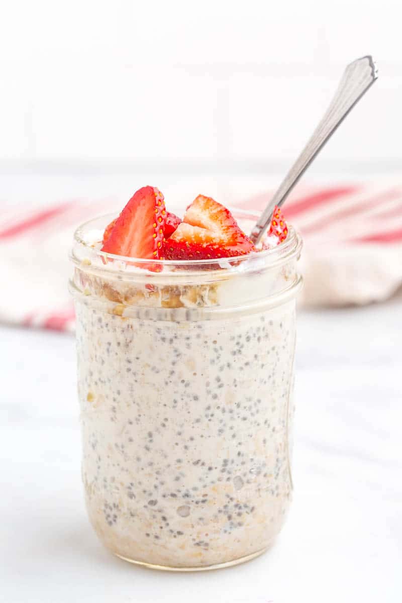 chia seed and oat mixture in mason jar with spoon, topped with sliced strawberries