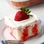 A piece of strawberry jello poke cake sits on a white plate with a fork on the side.