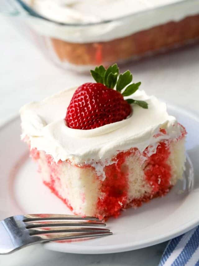 A piece of strawberry jello poke cake sits on a white plate with a fork on the side.