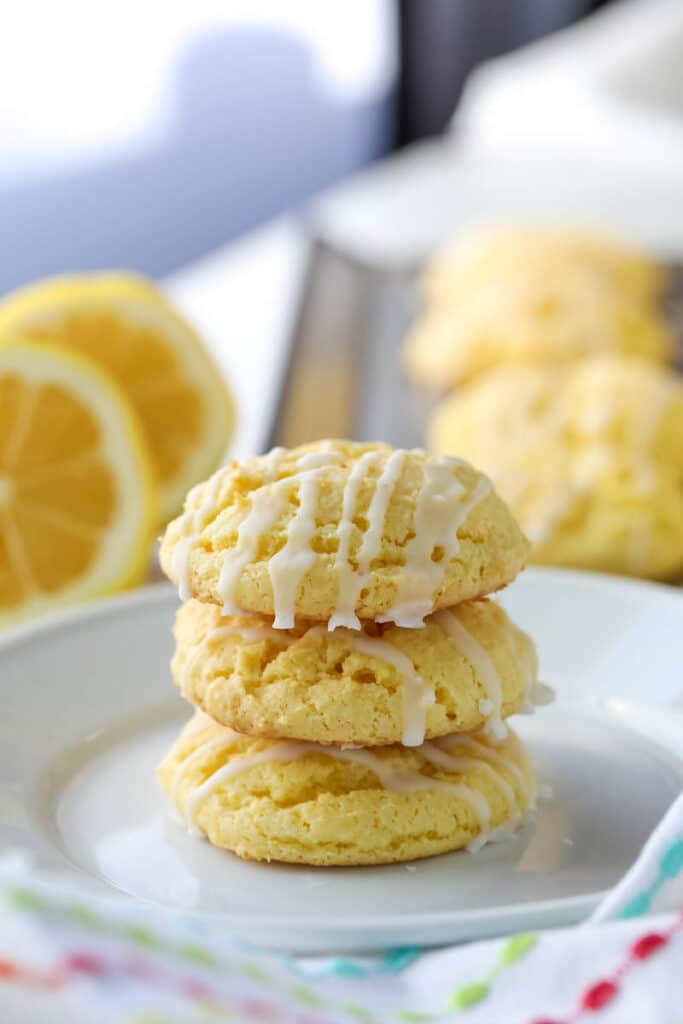 Three cake mix lemon cookies are stacked on top of each other on a white plate.