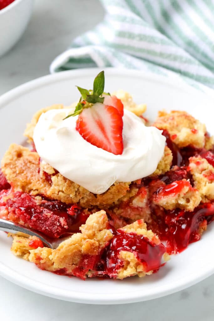 A serving of strawberry dump cake is garnished with whipped cream and a slice of strawberry.