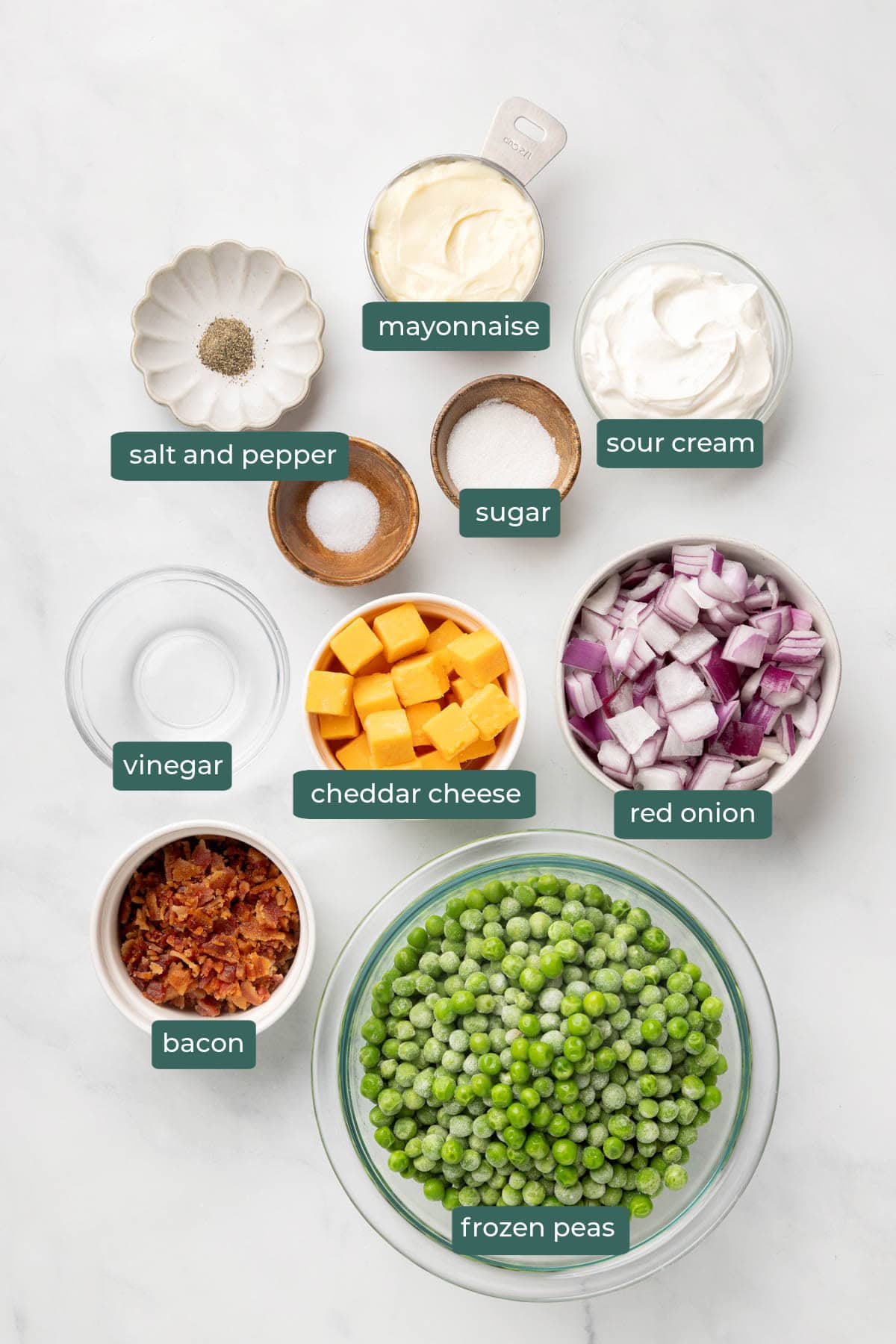 All of the ingredients for pea salad in bowls on a white countertop.