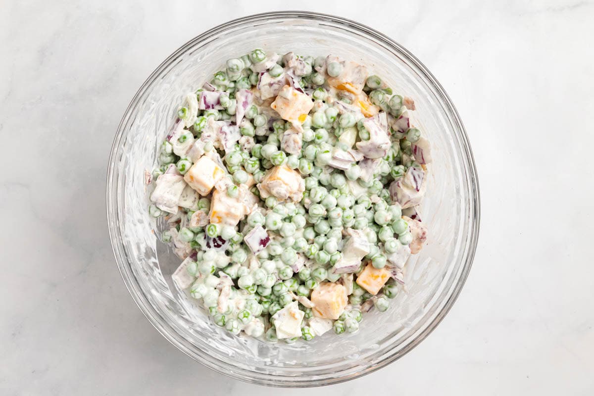 The finished sweet pea salad in a glass bowl on a white countertop.