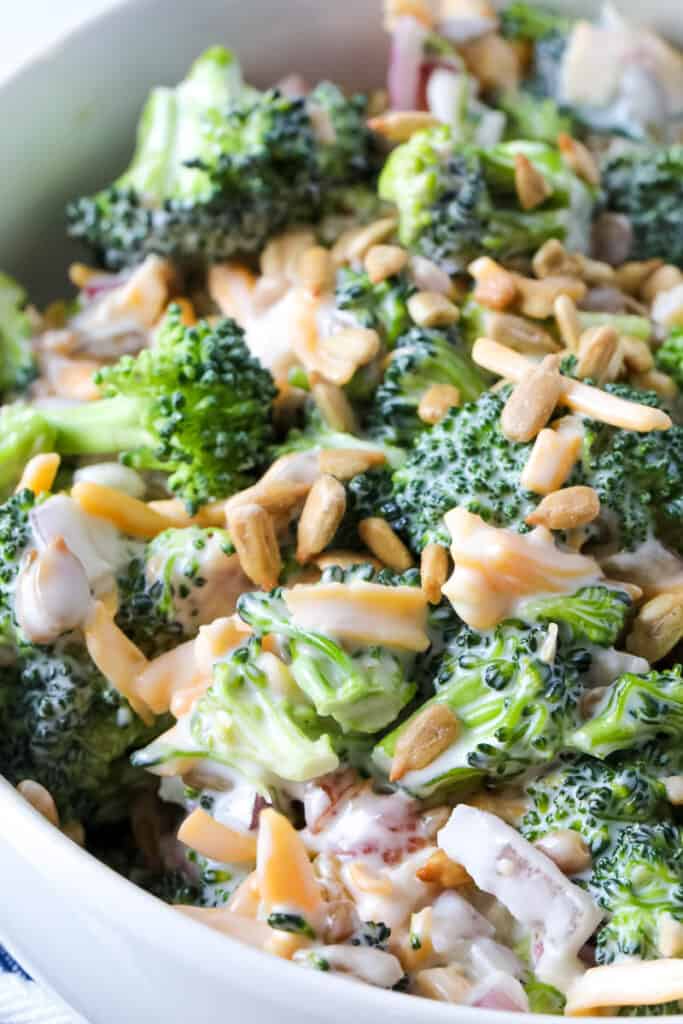 Close up of broccoli salad with creamy dressing and sunflower seeds in a white bowl.