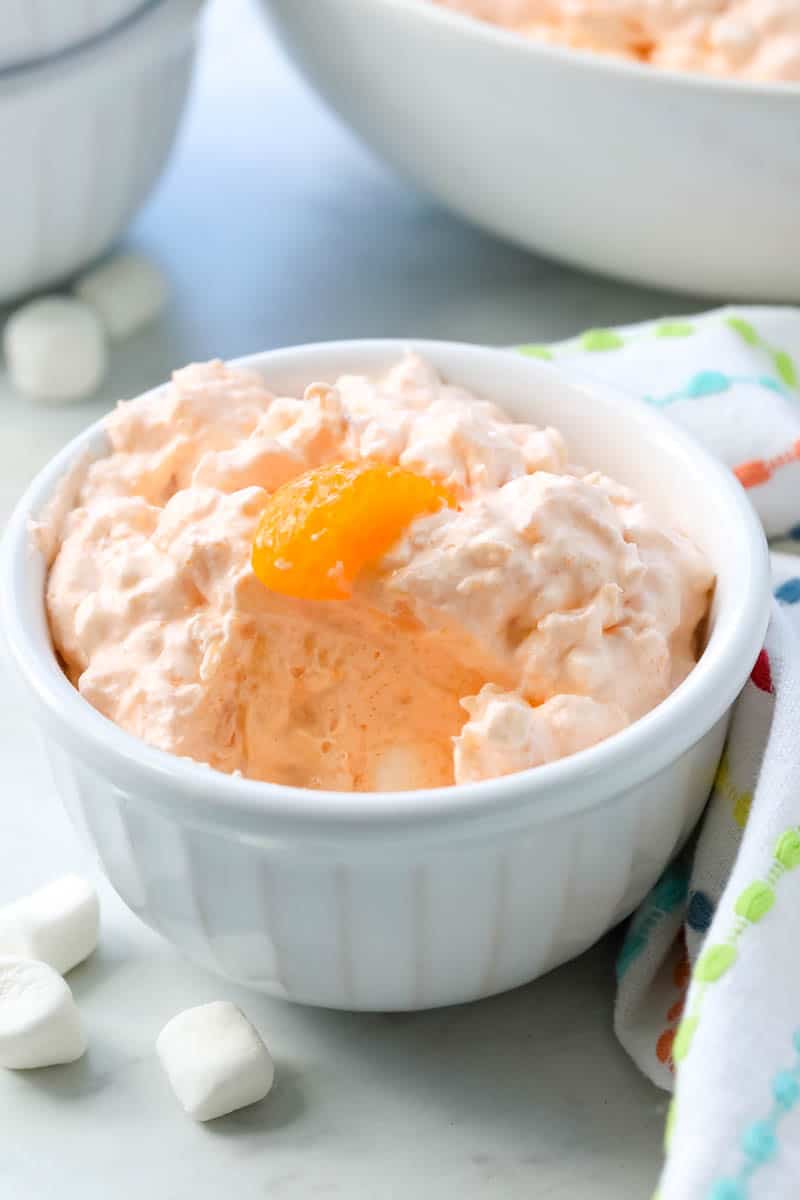 Orange fluff salad in a white ramekin with one mandarin orange on top.