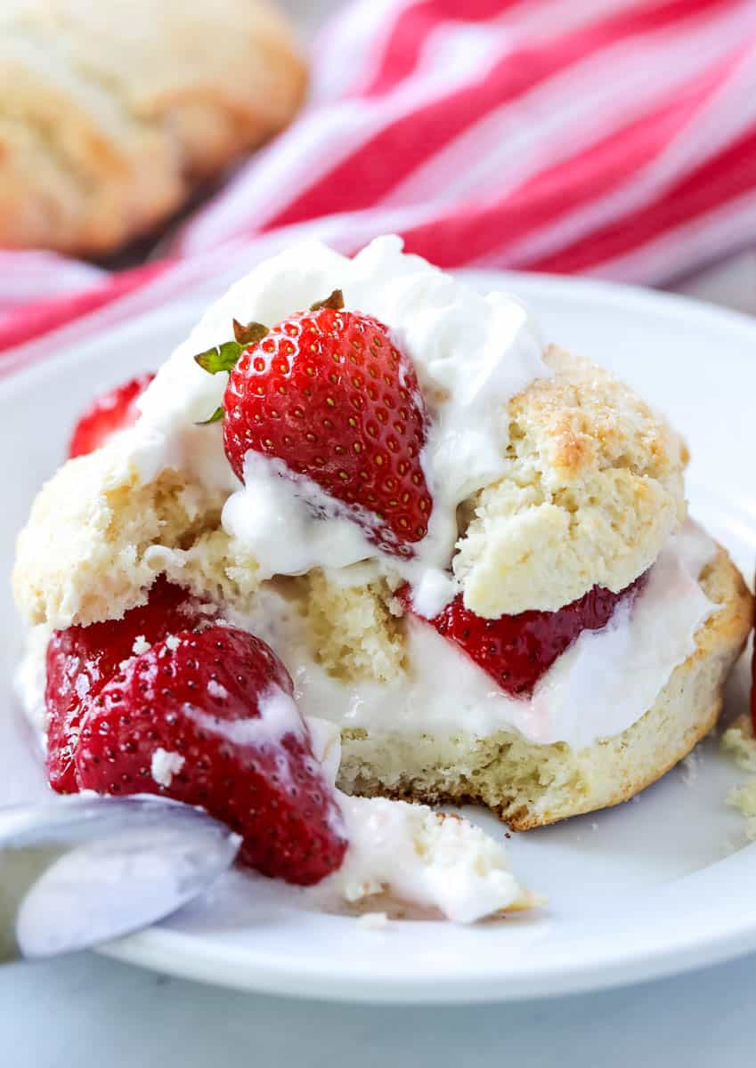 strawberry short cake with whipped cream on a white plate with a bite missing