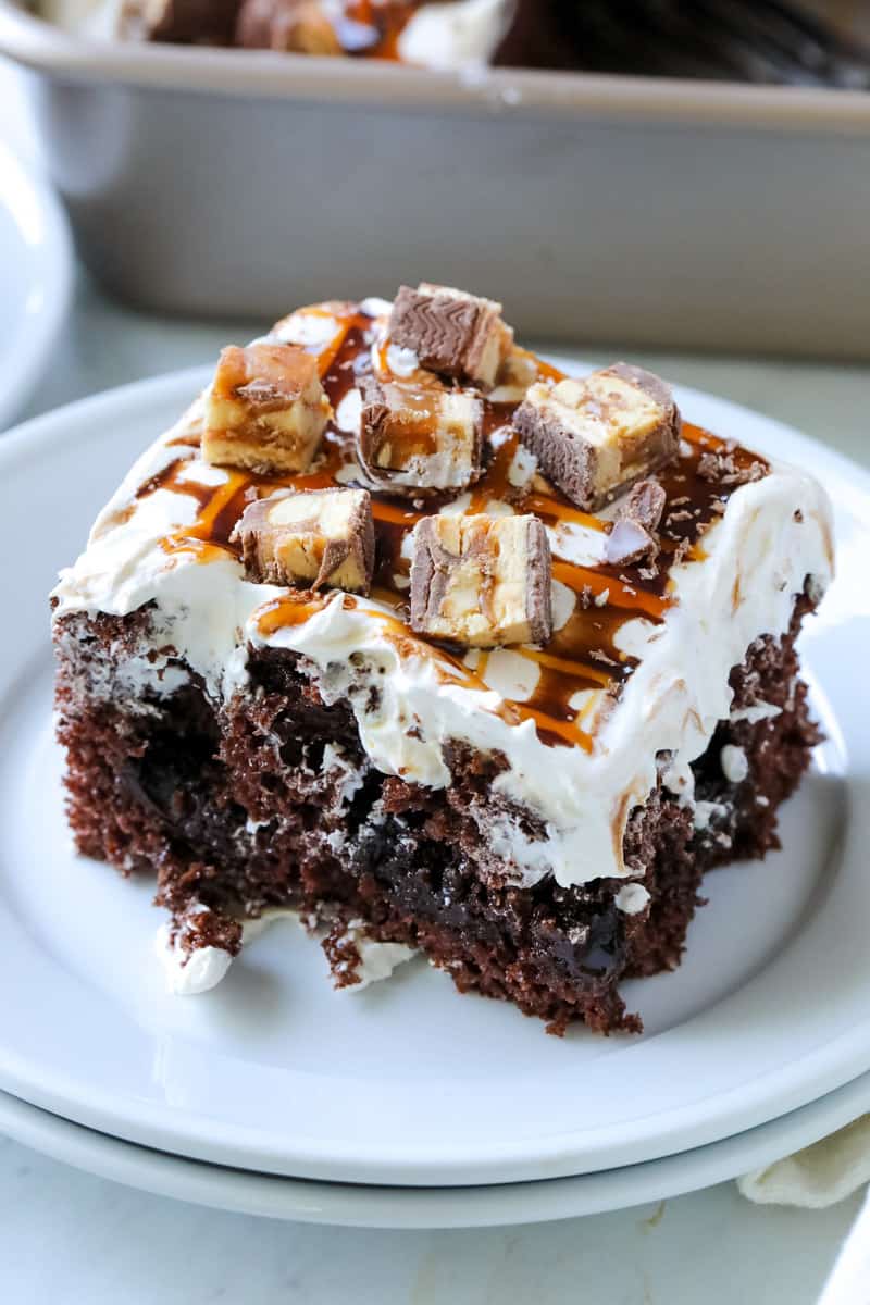 snickers poke cake on a white plate on a table