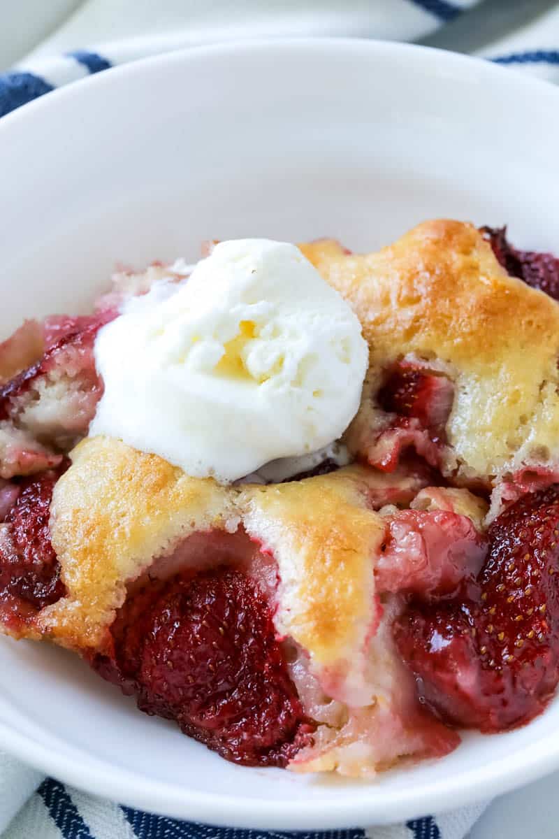 strawberry cobbler in a white bowl topped with vanilla ice cream.