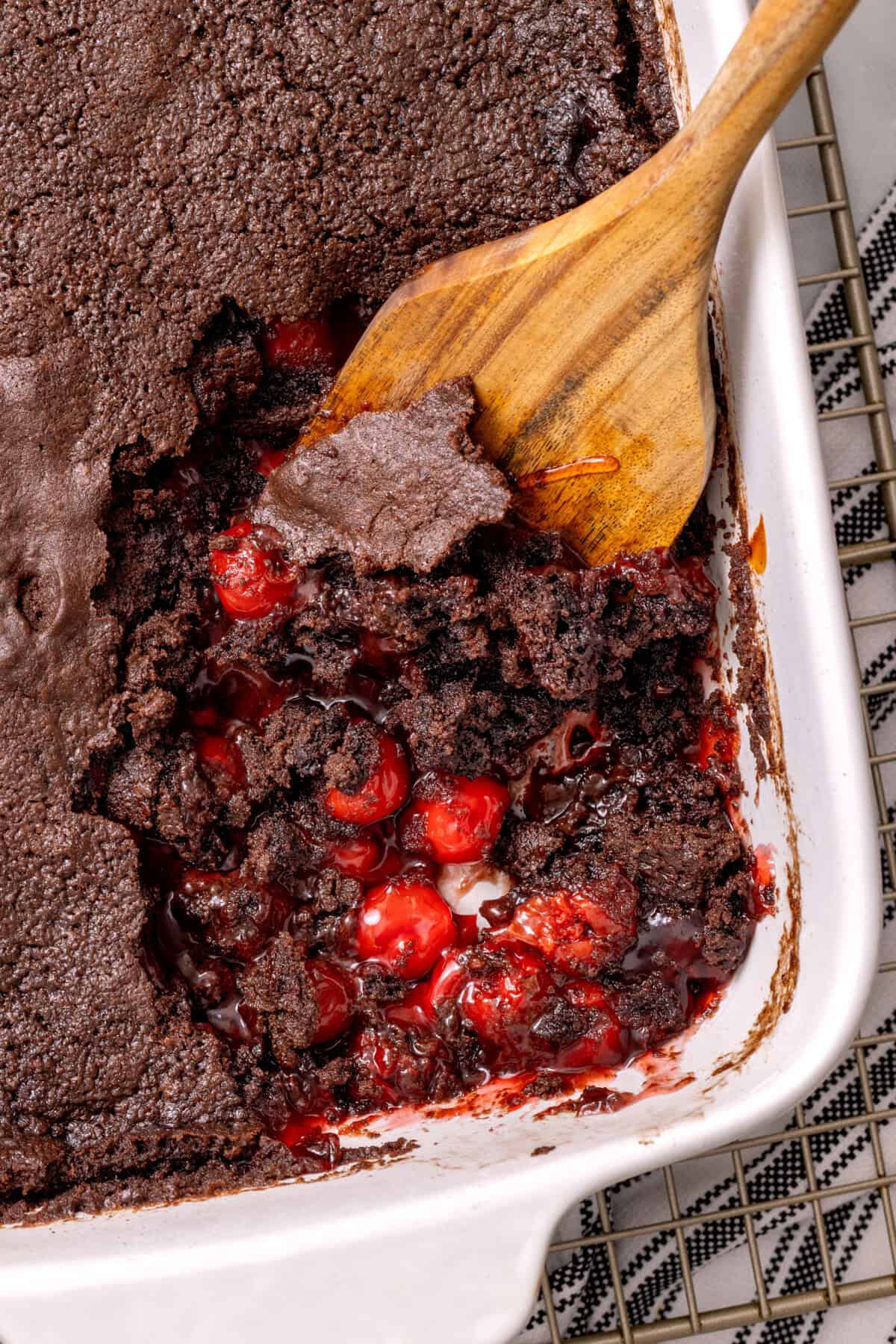 Wooden spoon scooping serving of chocolate cherry dump cake from pan.
