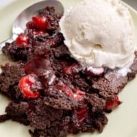 Chocolate cherry dump cake on a plate with a scoop of vanilla ice cream melting on top and a spoon on the side