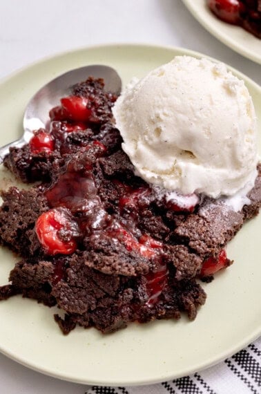Chocolate cherry dump cake on a plate with a scoop of vanilla ice cream melting on top and a spoon on the side