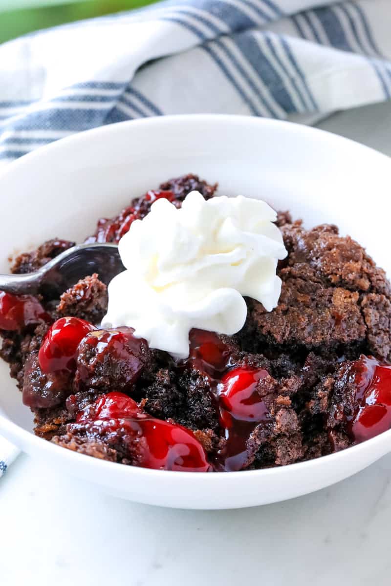 chocolate cherry dump cake in a white bowl and topped with whipped cream