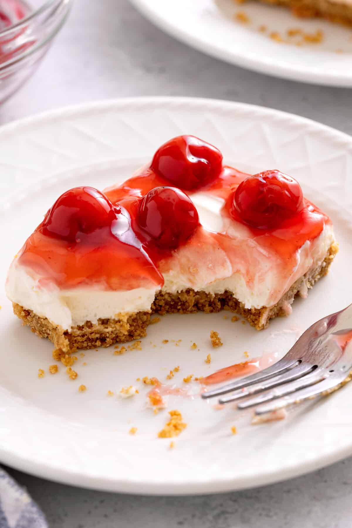 Slice of cherry no bake cheesecake on plate, with corner eaten.