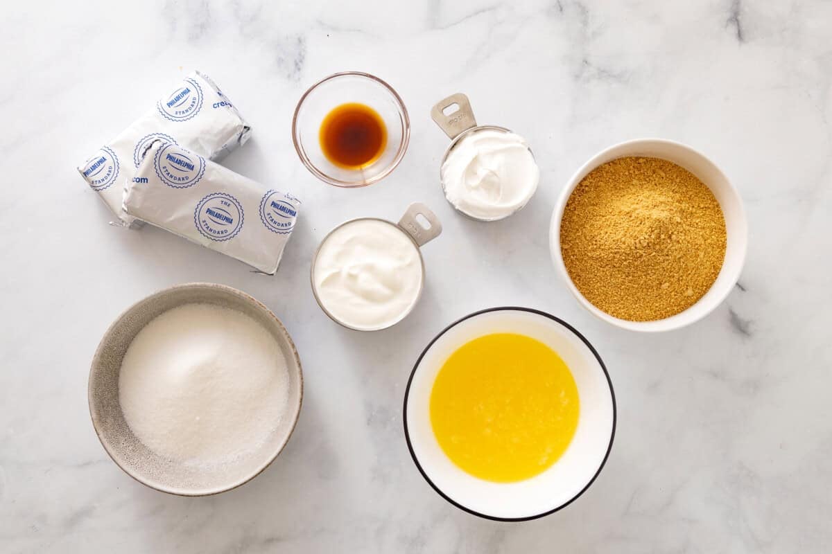 Ingredients for no bake cheesecake, including cream cheese, whipped cream, sugar, butter, graham cracker crumbs, vanilla.
