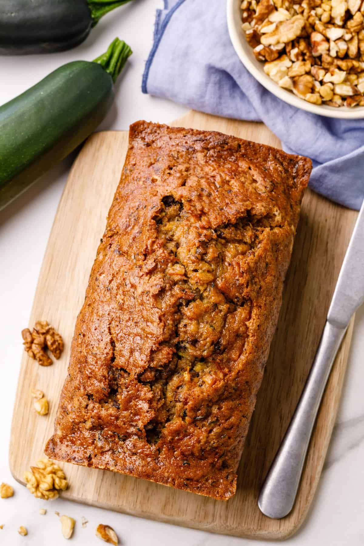 top down image of zucchini bread sitting on a wooden cutting board with a silver butter knife