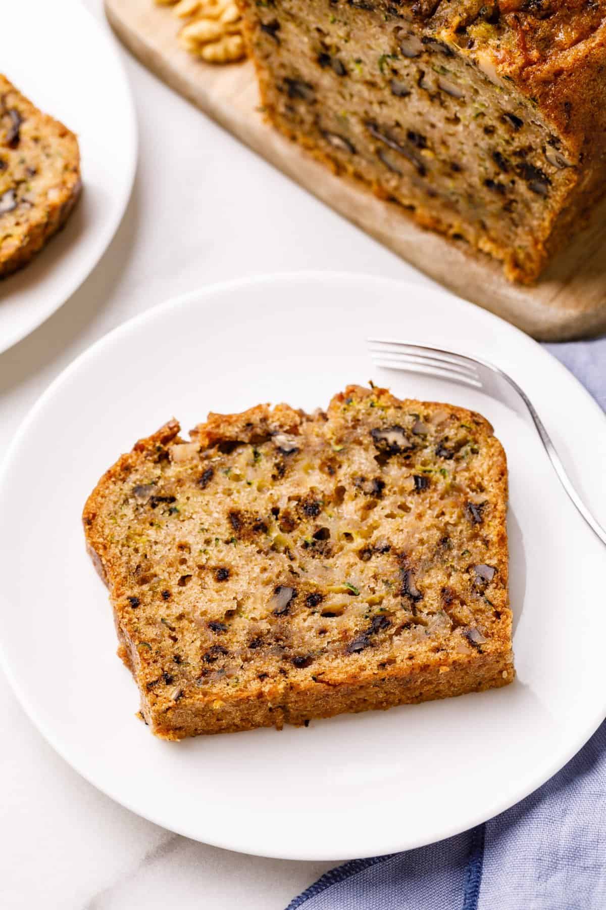 top down image of a slice of zucchini bread served on a white round plate with a silver fork