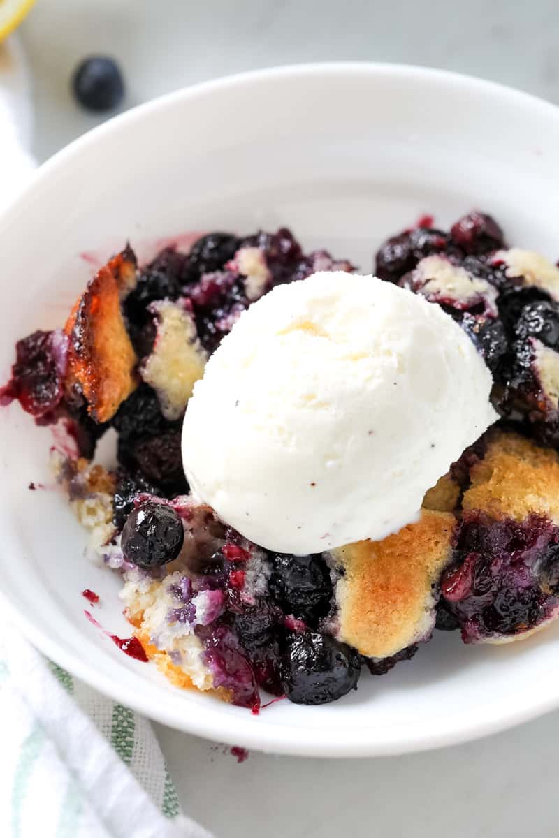 blueberry cobbler in a white bowl with a scoop of ice cream