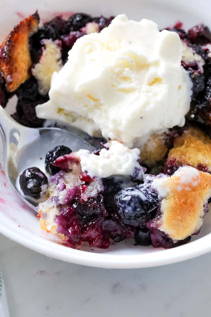 putting ice cream on top of baked blueberry dessert