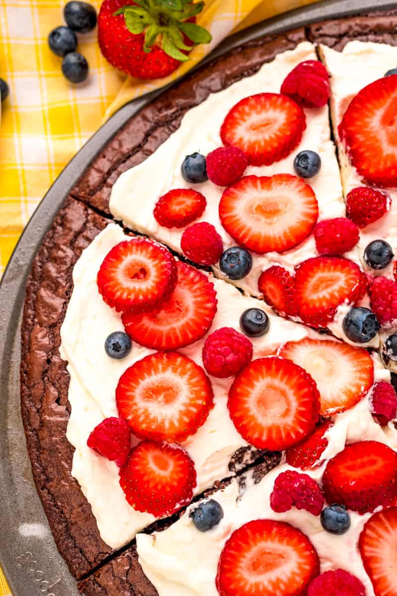 left side of a sliced brownie fruit pizza topped with raspberries, blueberries and sliced strawberries on the baking pan 