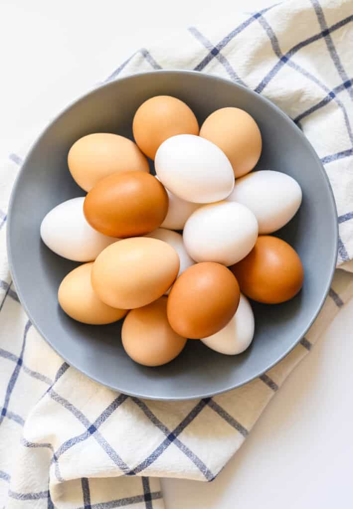 chicken eggs white and brown color in a gray plate on a checked kitchen towel on a white table. concept farm products and natural nutrition. vertical photo