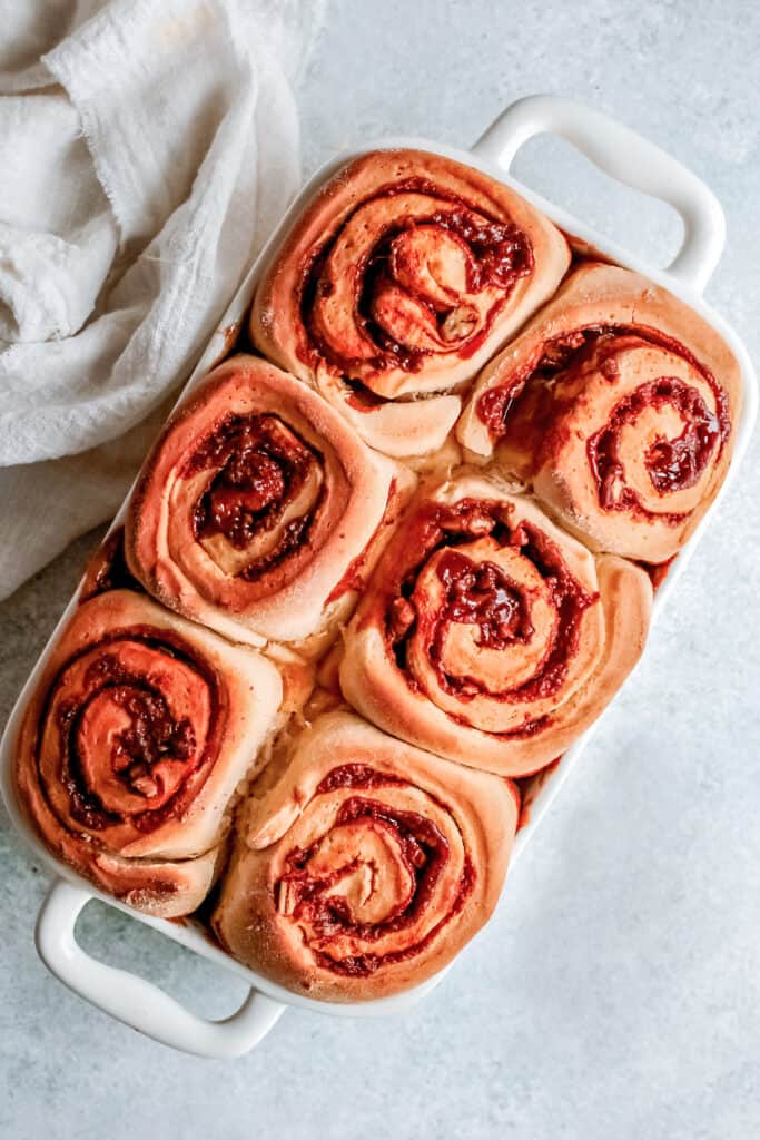 caramel pecan cinnamon rolls in a white casserole dish on a white countertop with a white linen cloth next to the cinnamon rolls