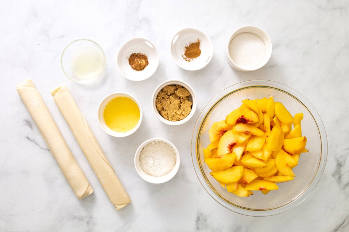 Ingredients for peach pie recipe, including pie crust, peaches, lemon juice, sugar, brown sugar, flour, nutmeg, cinnamon, egg.
