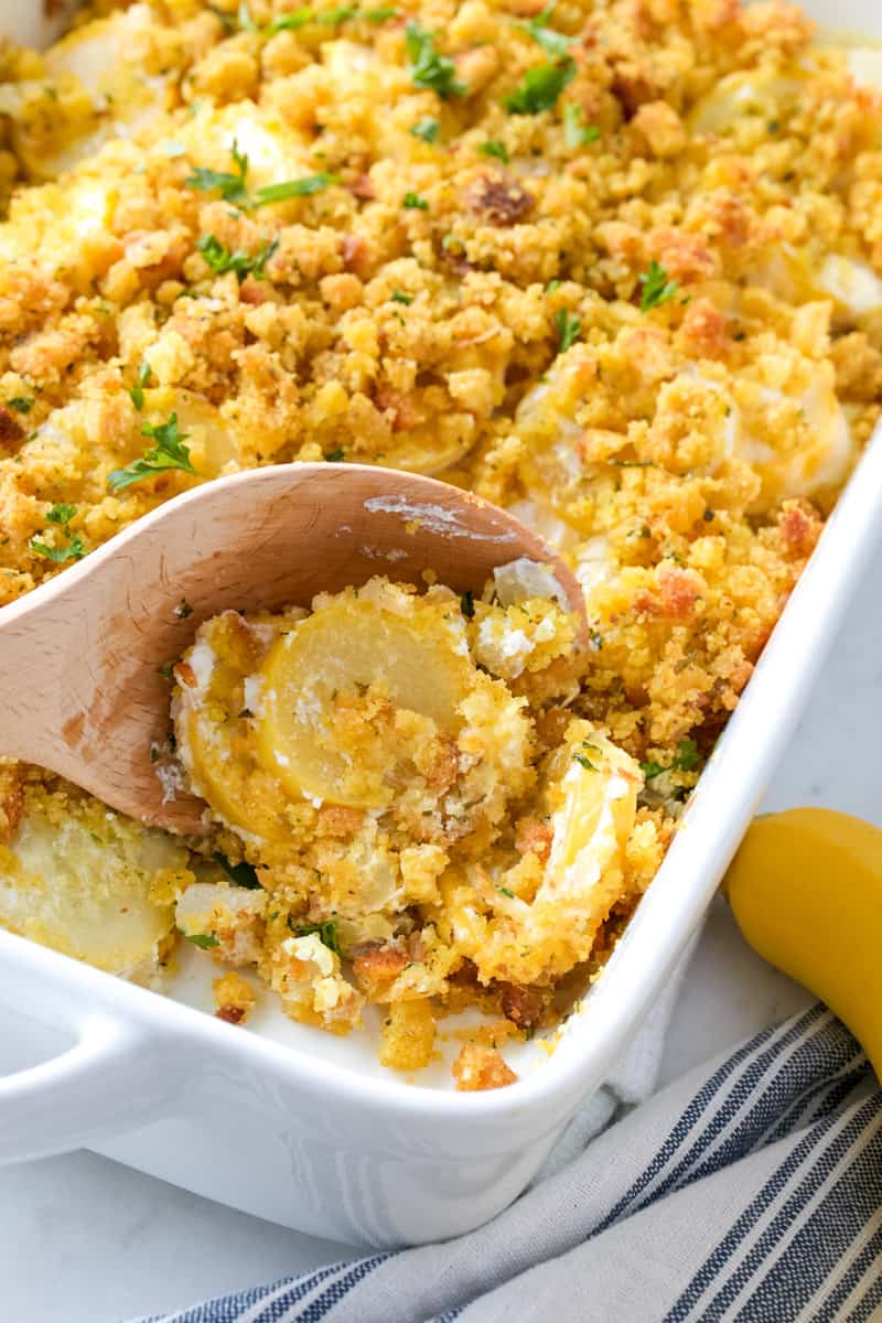 a wooden spoon serving up squash casserole from the corner of the baking dish 