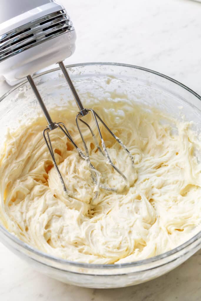 Bowl of cream cheese frosting with hand mixer.