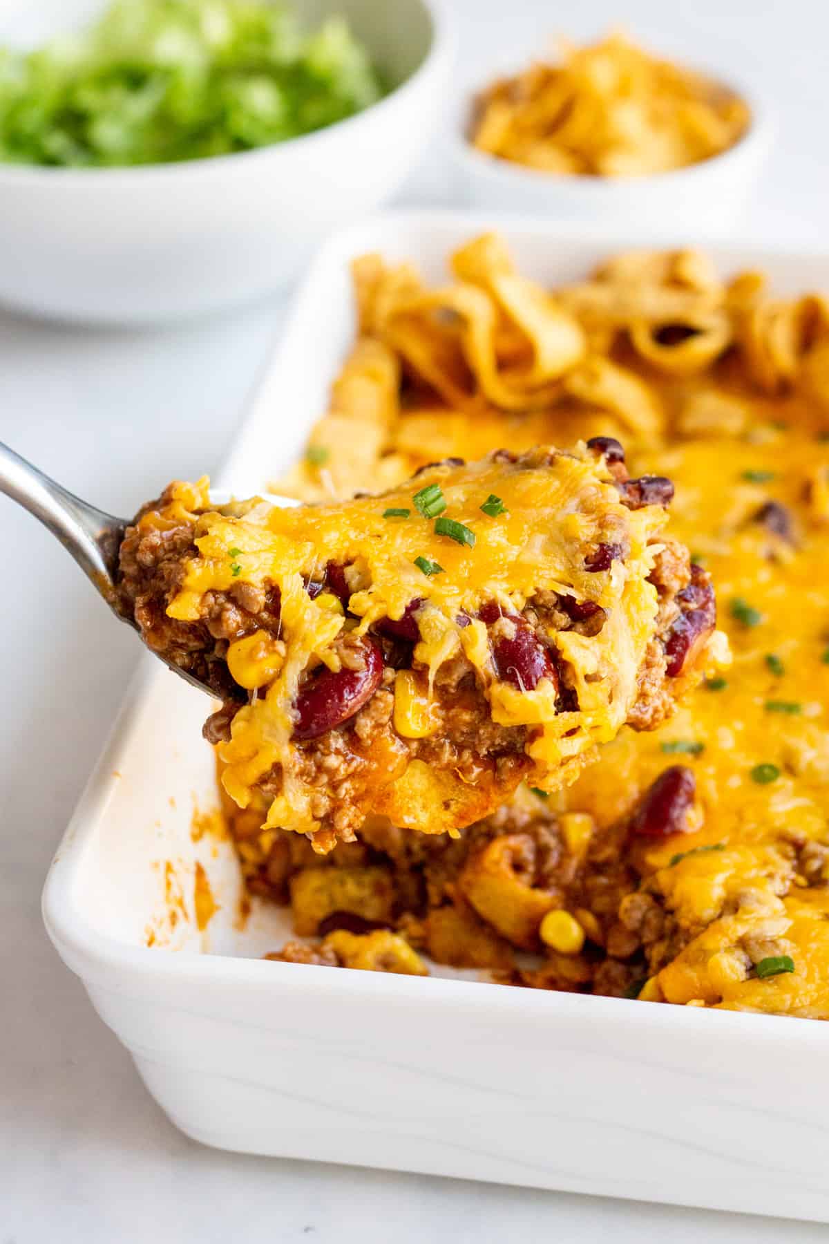 metal spoon scoop of frito pie from white casserole dish