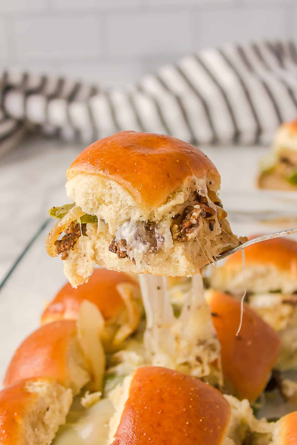 philly cheesesteak slider taken out of casserole glass dish sitting on a metal fork