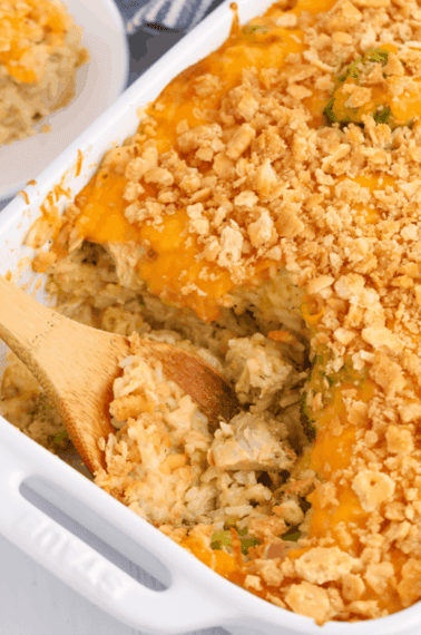 Cheesy chicken and rice casserole with a wooden spoon taking a scoop.