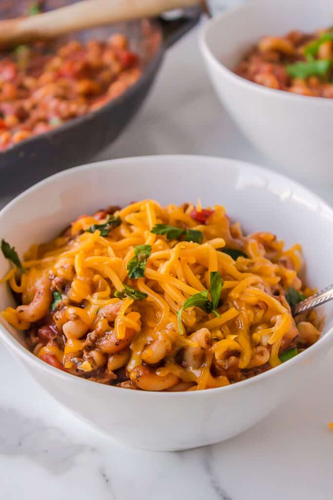 old fashioned goulash with cheddar cheese on top served in a white bowl
