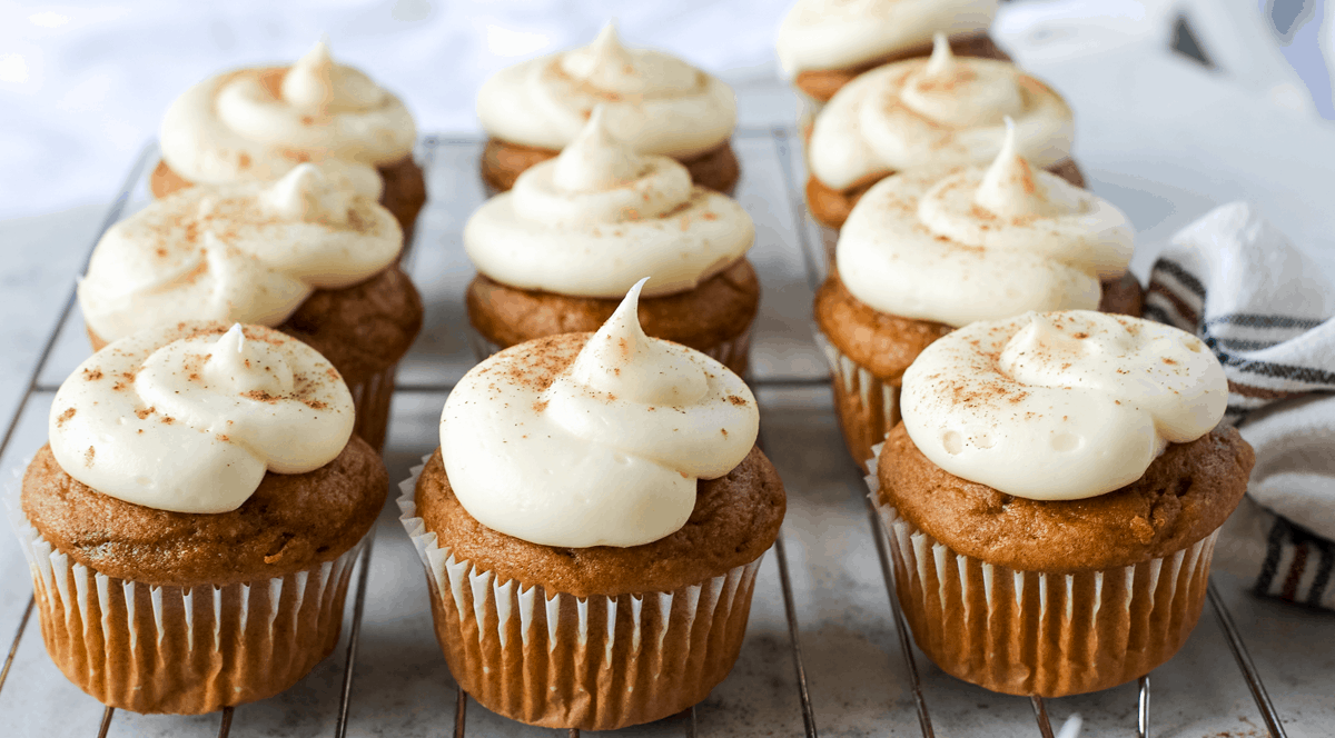 ten pumpkin spice cupcakes with cream cheese frosting on a metal cooling rack