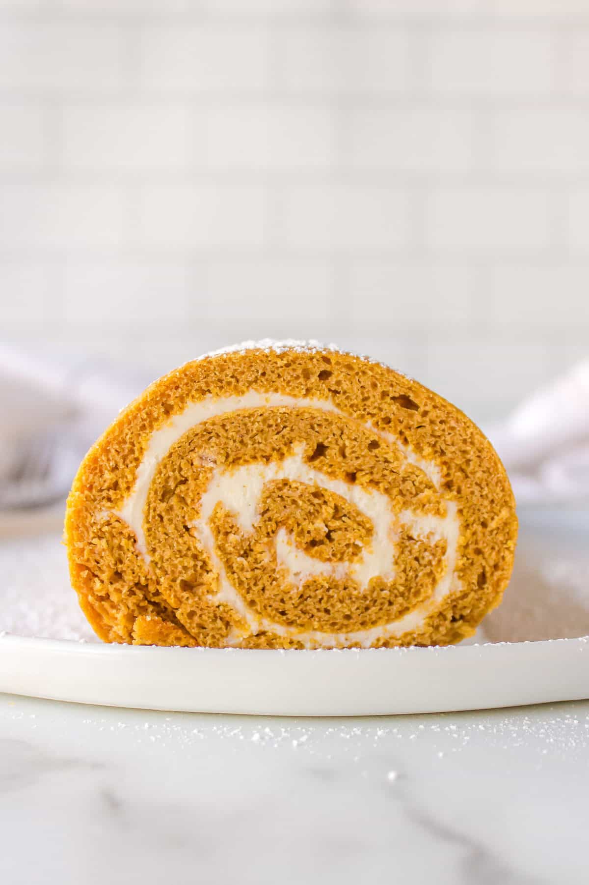sliced cross section of cake mix pumpkin roll with cream cheese frosting served on a white plate