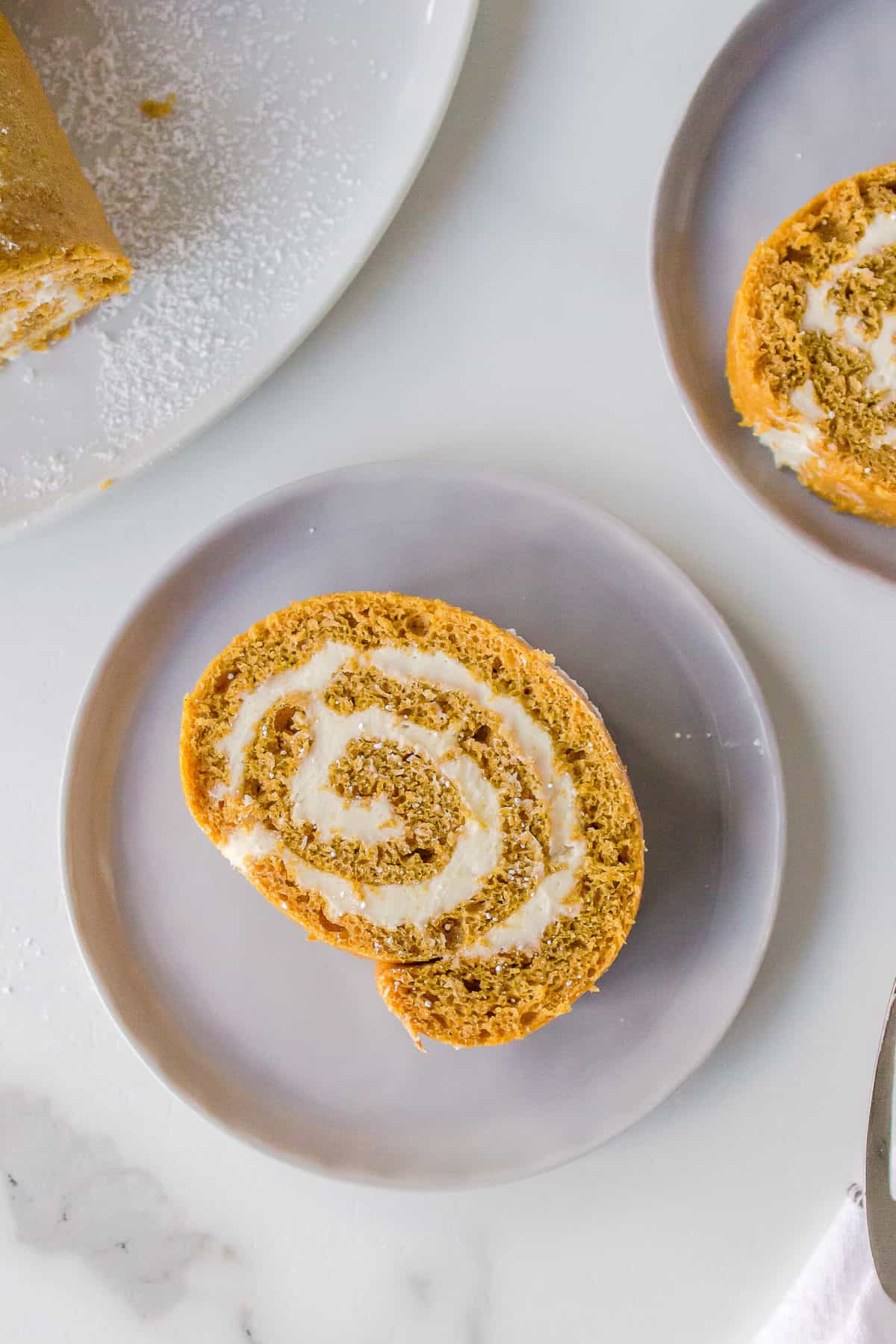 slice of a cake mix pumpkin roll with cream cheese frosting served on a taupe plate